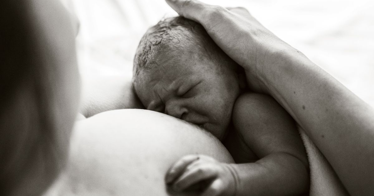 A black and white photo of a newborn baby attached to the mother's breast.